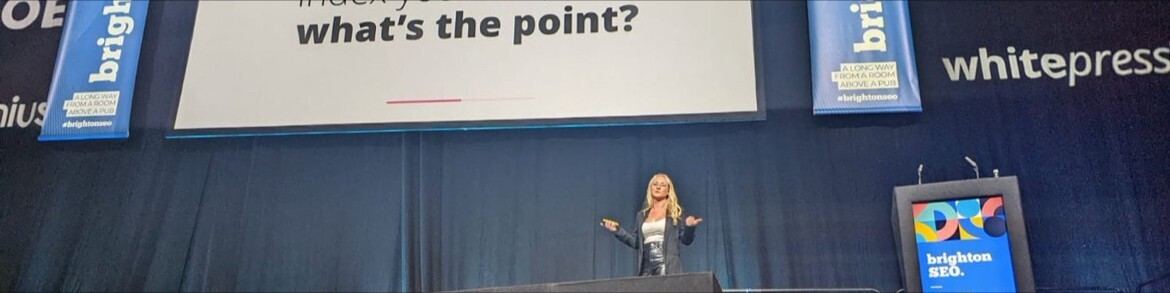 Sophie on stage at BrightonSEO, under a slide that reads: what's the point?