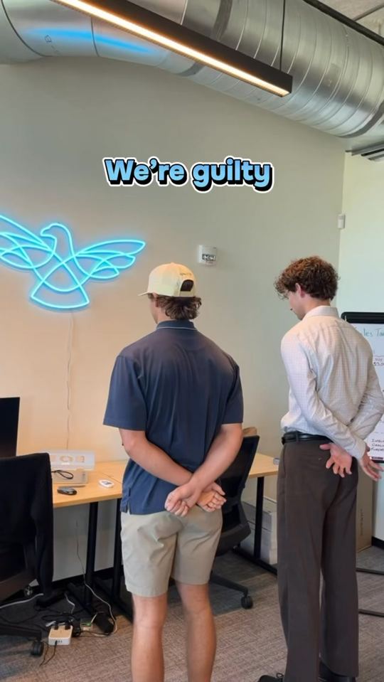 StudioHawk team members standing in the office under a neon hawk logo, with the caption We're guilty